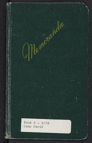 Photo of a small green notebook with the word "Memoranda" written in gold text on the cover. At the bottom of the cover is a faded white label that reads "Book D - 9/78, Camp David." The notebook contains notes from the Camp David Accords. It belonged to Hal Saunders.