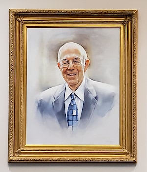 Painted portrait of Hal Saunders from the shoulders up. He is a white man wearing glasses, a blue suit, and a white collared shirt. He is smiling, and his blue checkered tie has one square that features the silhouette of a dove.