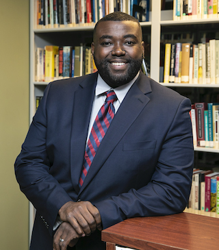 Charles Chavis standing in a library, smiling, wearing professional attire