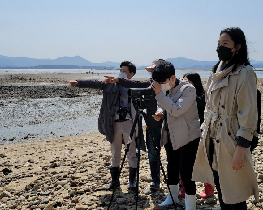 Kim on a beach operating a camera with a group of people.