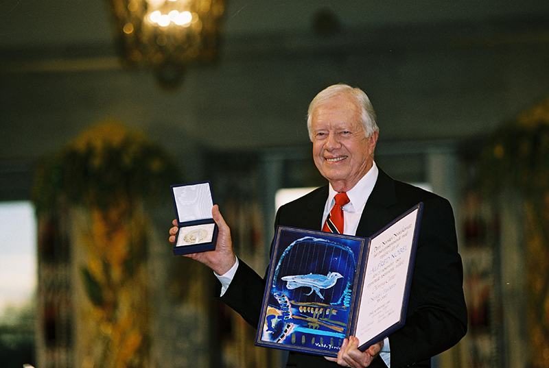 Former President Jimmy Carter smiling and holding the Nobel Peace Prize