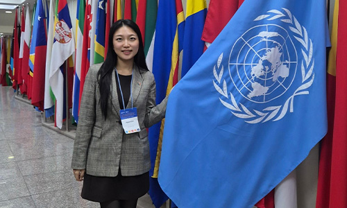 Hyoid Kim standing with the United Nations flag and the flags of member nations