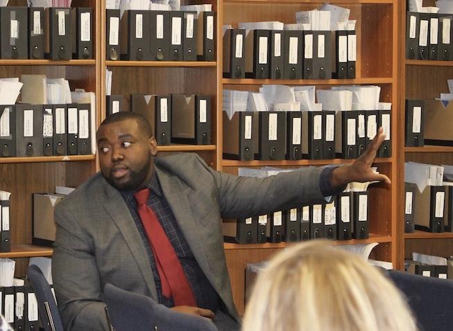 Charles Chavis speaking at a dialogue event. He is seated with his left arm outstretched.