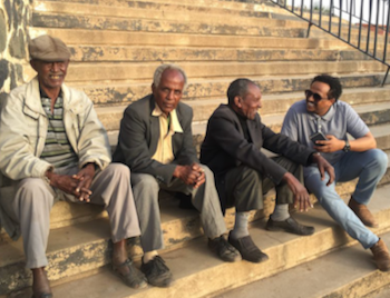 Three older Black men and one young Black man chat while sitting on steps.