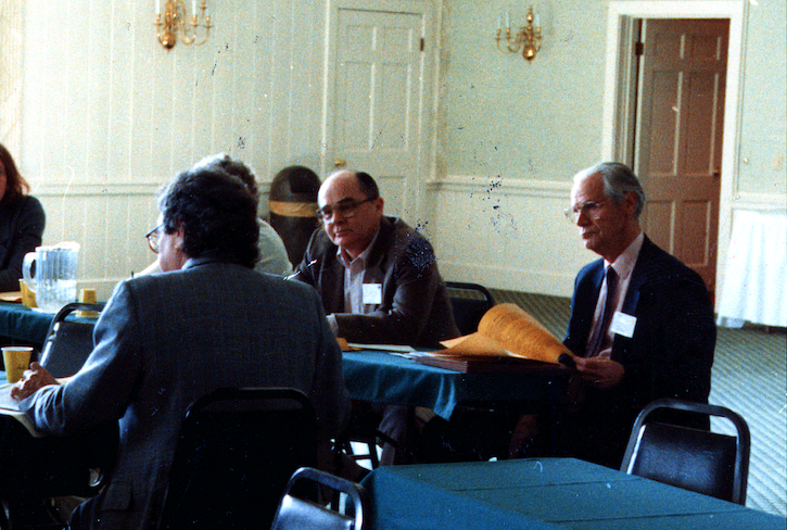 Old photo of people around a table during an academic conference. Identifiable are Jim Laue and John Burton.