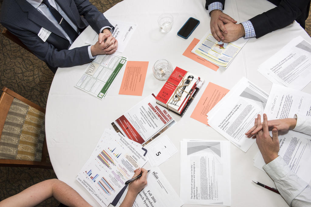 Photo from above of a roundtable with the hands of people sitting at the table and research flyers across the table.