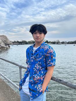 Johnathan Fang standing in front of the tidal basin in Washington DC with cherry blossoms and Jefferson Memorial in background